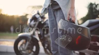 美丽的年轻红发女子摩托车手与她的摩托车和头盔。 日落或日出时在街上。 女摩托车手