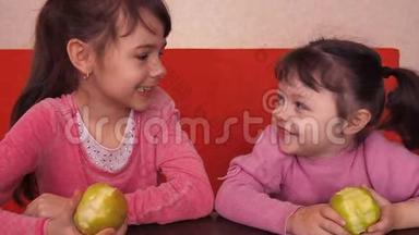 孩子们吃<strong>苹果</strong>。 两个姐妹坐在橙色的沙发上吃<strong>黄</strong>色的<strong>苹果</strong>。