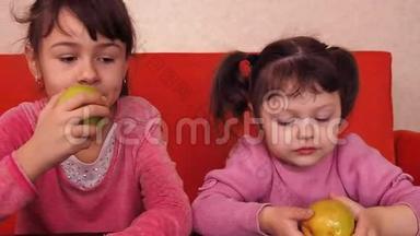 孩子们吃苹果。 两个姐妹坐在橙色的沙发上吃黄色的苹果。