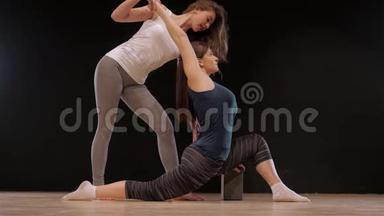 瑜伽教练帮助学生伸展肩膀。 快乐运动适合女孩