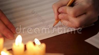 学生写音乐：音乐家用铅笔在带有烛光的音乐书中作曲.. 音乐家的特写