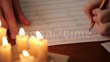 学生写音乐：音乐家用铅笔在带有烛光的音乐书中作曲.. 音乐家的特写