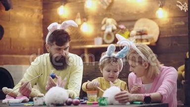 母亲、父亲和儿子<strong>正在</strong>画鸡蛋。 幸福的家庭<strong>正在</strong>为复活节做<strong>准备</strong>。 可爱的小男孩穿着兔子