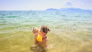 金发母亲挽着小女儿在蔚蓝的大海里