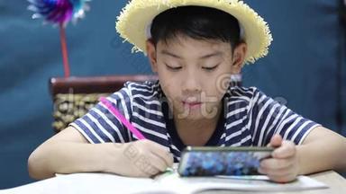 一个亚洲小男孩微笑着看着手机屏幕和绘画