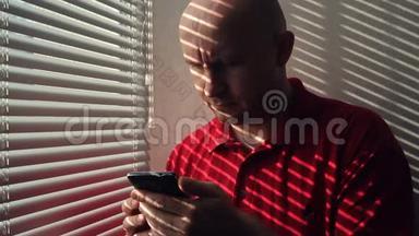 一个带智能手机的人站在窗户边带百叶窗