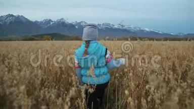 小女孩走在麦田里。 孩子奔跑的背景是美丽的山脉和白雪覆盖的山峰。 儿童