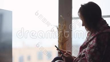坐在窗台上坐在窗台上，一边用手机看着窗户的悲伤女人。 1920x1080。