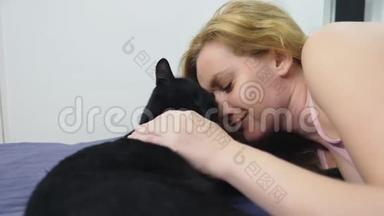 带猫的女孩。 美丽的金发女孩躺在床上抚摸她的黑猫。 关心动物。 爱宠物