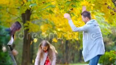 在秋日的户外活动中，一个微笑的年轻家庭把树叶扔来扔去