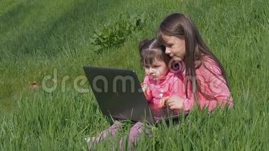 带着笔记本电脑在绿草上的<strong>小</strong>女孩。 阳光明媚的一天，公园里的姐妹们。 穿<strong>粉色</strong>衣服的<strong>小</strong>女孩带着笔记本电脑。