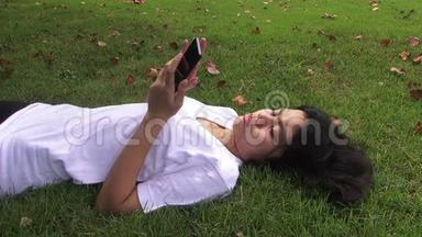秋天公园里，一个快乐的年轻女子<strong>坐在树下</strong>，一边用手机聊天。