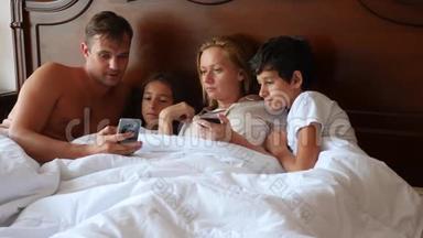 一个幸福的家庭躺在床上看着他们的智能手机上的东西。 4K，慢动作。