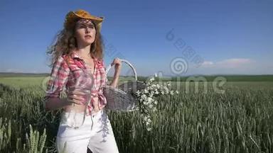 年轻的女人带着花篮和一瓶水走着，背景上有蓝天的麦田。 慢慢慢慢