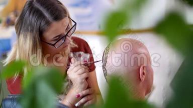 一个女孩，纹身大师，迈亨迪艺术家在秃顶白种人的头皮上画指甲花纹身，穿着一件蓝色衬衫