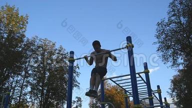 强壮的肌肉男在公园里做肌肉锻炼。 年轻运动员在户外水平杆上做下巴练习。 健身
