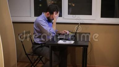 一个疲惫的商人晚上工作到很晚，办公室里拿着一台笔记本电脑，写了一份财务报告