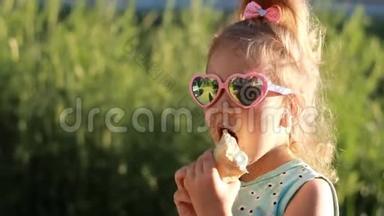在阳光明媚的夏天，小女孩戴着太阳镜吃冰淇淋。