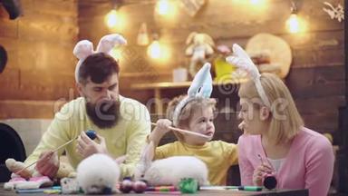 母亲、父亲和儿子正在画复活节彩蛋。 幸福的家庭正在为复活节做准备。 可爱的小男孩穿着