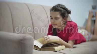 十几岁的女孩躺在沙发上看书。 躺在沙发上看书的女孩