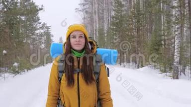 女游客走在冬天的森林路上，肩上背着一个背包。