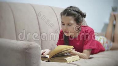 十几岁的女孩躺在沙发上看书。 躺在沙发上看书的女孩