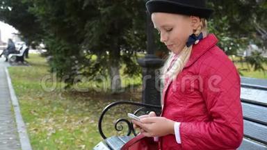 今年秋天，城市公园的一位年轻女孩在智能手机上使用应用程序坐在长椅上