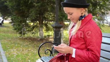 <strong>今年</strong>秋天，城市公园的一位年轻女孩在智能手机上使用应用程序坐在长椅上