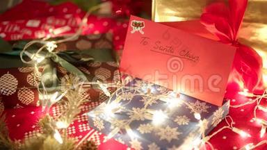 一个红包和致圣诞老人的信躺在圣诞树下的礼盒和明亮的灯光下