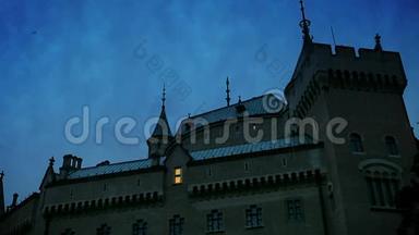 中世纪的城堡场景：随着黄昏的降临，窗户里逐渐出现了灯光。 一<strong>群鸟</strong>从屋顶上<strong>飞过</strong>。