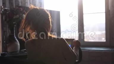 年轻的黑发女人在家靠窗的自行车模拟器上练习，在日落时用镜头看城市