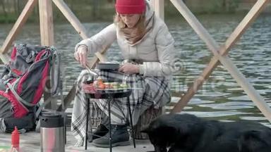 女游客穿着温暖的衣服在河岸附近的桥上背着背包，准备烤蔬菜，喂饭