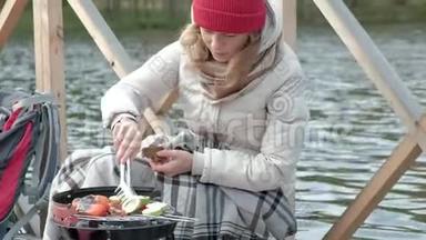 女游客穿着温暖的衣服在河岸边的桥上背着背包，准备烤蔬菜，喂饭
