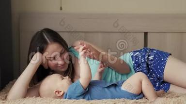 母亲和孩子在一张白色的床上。 妈妈和小男孩穿着尿布在阳光明媚的卧室里玩。 家长和小孩放松