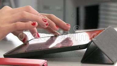 女人的双手用<strong>鲜红</strong>的指甲在平板上工作。
