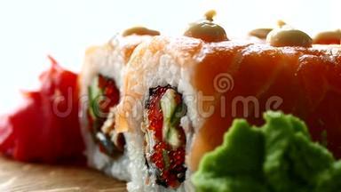 美味可口的寿司。 寿司配三文鱼片和新鲜黄瓜。 木头上有红姜和青芥末
