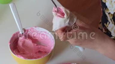 一个女人把粉红色的奶油放进糕点袋里。 下一个海绵蛋糕铺上白色奶油。