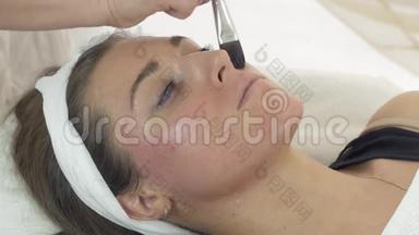 美容师的双手在美容院的女孩脸上贴着润肤露。
