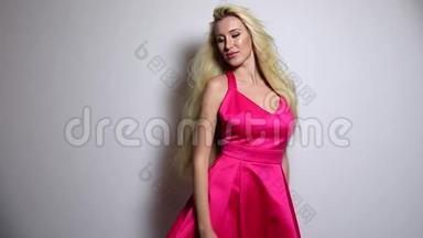 漂亮的女人穿着粉红色的连衣裙在演播室背景下摆姿势。 慢动作录像。