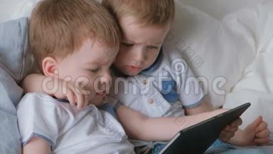 带平板电脑的孩子。 两个男孩双胞胎蹒跚学步，看着躺在床上的平板电脑。