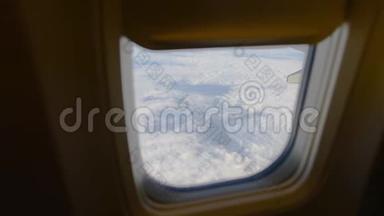 飞机机翼通过飞机窗口的视图。 在云层之上飞行。