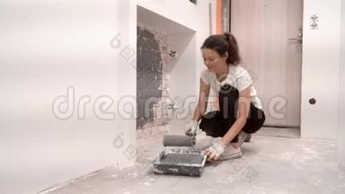 蹲着的女人滚出油漆滚筒，用灰色油漆砖墙。