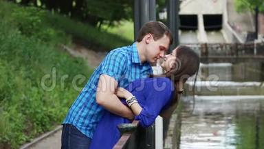 年轻人倚着女人，在公园的小河边亲吻她