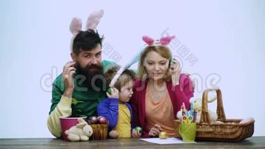 母亲、父亲和儿子<strong>正在</strong>画鸡蛋。 幸福的家庭<strong>正在</strong>为复活节做<strong>准备</strong>。 可爱的小男孩穿着兔子