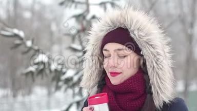 美丽的年轻女孩在冬天的公园里喝热水瓶里的咖啡。