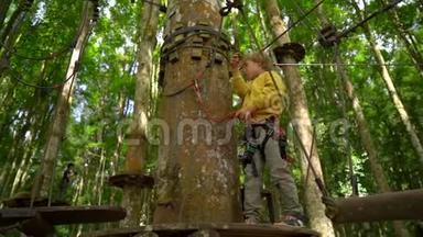 一个穿着安全装备的小男孩在森林探险公园的树梢上爬上了一条路线。 他爬上去