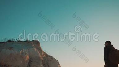 一位男士游客的剪影在日落的生活方式冒险中爬上山顶。 剪影