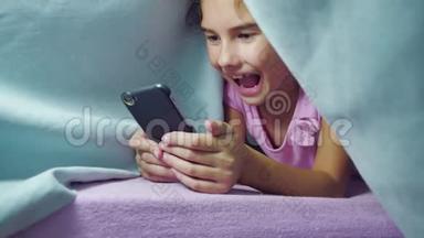女孩少年和狗在夜里在智能手机里玩毯子。 <strong>睡前</strong>的小女孩躺在床上冲浪