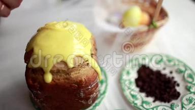复活节蛋糕上有黄色的糖霜和五颜六色的花洒在白色的桌子上。 给女孩浇糖蛋糕