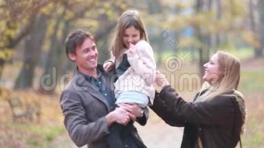 一家人在公园里散步，爸爸抱着女儿，妈妈逗她开心